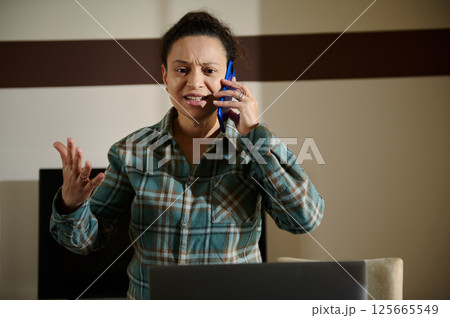 Woman Expressing Frustration While on a Phone Call in Home Office Setting Woman Expressing Frustration While on a Phone Call in Home Office Setting 125665549