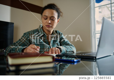 Woman Working on Laptop and Notes in Home Office Setting Woman Working on Laptop and Notes in Home Office Setting 125665581
