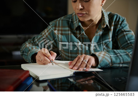 Focused Woman Writing Notes in a Journal at Her Desk Focused Woman Writing Notes in a Journal at Her Desk 125665583