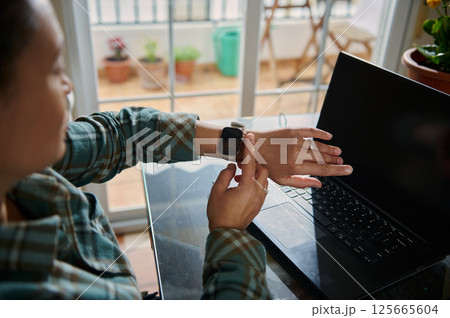 Person Using Smartwatch While Working on Laptop at Home Office 125665604