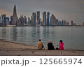 Doha Qatar skyline from corniche promenade sunset shot showing dhows in Arabic gulf with Qatar flag and people sitting 125665974