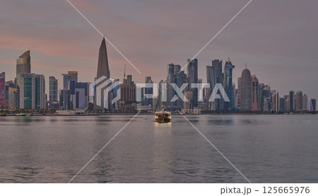 Doha Qatar skyline from corniche promenade sunset shot showing dhows in Arabic gulf with Qatar flag 125665976