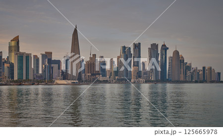 Doha Qatar skyline from corniche promenade sunset shot showing dhows in Arabic gulf with Qatar flag 125665978