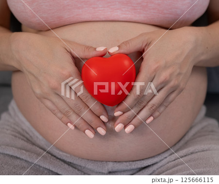 Caucasian pregnant woman holding heart on belly background. Third trimester. Caucasian pregnant woman holding heart on belly background. Third trimester. 125666115