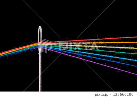 multi-colored threads for sewing in the form of a rainbow pass through an antique needle on a black background 125666196