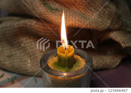 Natural Wax Candle Burns In Glass Cup With Wheat Grain On Burlap Background Natural Wax Candle Burns In Glass Cup With Wheat Grain On Burlap Background 125666467