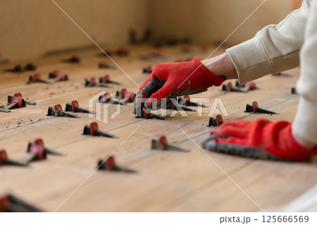 Man Installing Tile Leveling System Components on The Tiled Floor. Man Installing Tile Leveling System Components on The Tiled Floor. 125666569