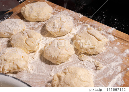 Irregularly shaped dough pieces dusted with flour rest on a wooden surface, ready for baking or cooking. 125667132