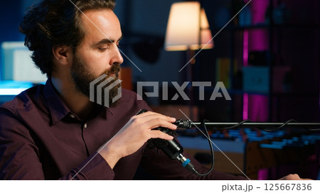 Portrait of ASMR artist uses quality mic in studio to do anti stress video, whispering sounds. Happy man using professional microphone to get sleep inducing high quality audio for meditation, camera A Portrait of ASMR artist uses quality mic in studio to do anti stress video, whispering sounds. Happy man using professional microphone to get sleep inducing high quality audio for meditation, camera A 125667836