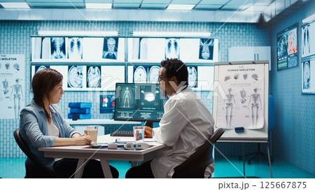 General practitioner presenting the diagnostic report at checkup with patient, discussing about treatment plan. Medic showing x ray imaging and scans on computer, medical results. Camera B. 125667875