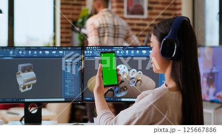 Asian freelancer developer working with headphones and chroma key screen, creating a new prototype for manufacturing industry. Female 3D modeling engineer at her home office. Camera B. 125667886