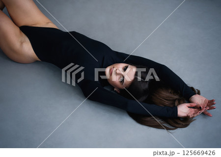 Beautiful slim brunette woman with perfect body in black bodysuit posing on grey studio background. Beautiful slim brunette woman with perfect body in black bodysuit posing on grey studio background. 125669426