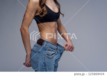 Woman with perfect body demonstrates weight loss, slimming by wearing old big jeans Woman with perfect body demonstrates weight loss, slimming by wearing old big jeans 125669434
