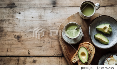 Overhead view of avocado toast, sliced avocado, fried egg, and matcha tea on a wooden board and table. Rustic and healthy breakfast layout AI generated 125670239