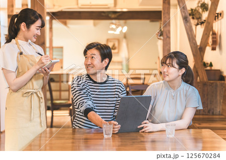 カフェ・レストラン・飲食店でタブレットを使ってメニューを注文・セルフオーダーする男女と説明する店員 カフェ・レストラン・飲食店でタブレットを使ってメニューを注文・セルフオーダーする男女と説明する店員 125670284