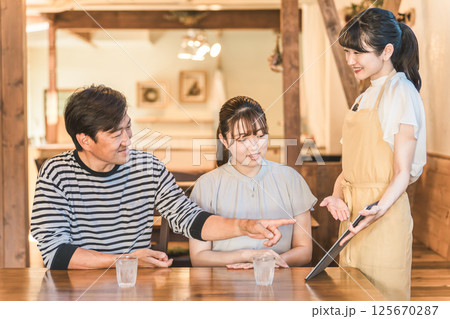カフェ・レストラン・飲食店でタブレットを使ってメニューを注文・セルフオーダーする男女と説明する店員 125670287