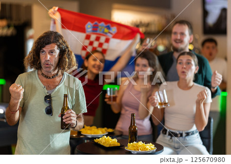 Sports supporters with flag of Croatia, rejoicing winning game with beer and snacks in pub 125670980