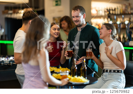 Happy mens and womens drinking beer and eating crisps, laughing and spending time together in bar Happy mens and womens drinking beer and eating crisps, laughing and spending time together in bar 125670982