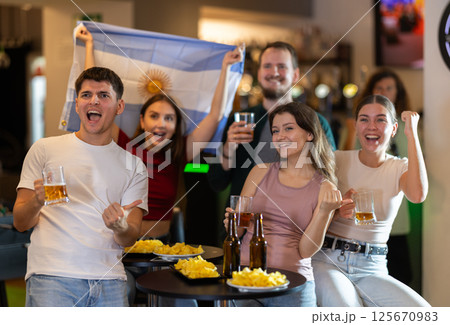 Group of emotional Argentine fans with the national flag watch the match on TV with interest and actively comment Group of emotional Argentine fans with the national flag watch the match on TV with interest and actively comment 125670983