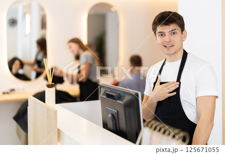 Male employee of barbershop stands near reception desk of salon, waits for visitors Male employee of barbershop stands near reception desk of salon, waits for visitors 125671055