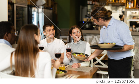 Male waiter brings food for company in restaurant Male waiter brings food for company in restaurant 125671056