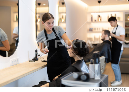 Young female hairdresser giving haircut to adult woman Young female hairdresser giving haircut to adult woman 125671068