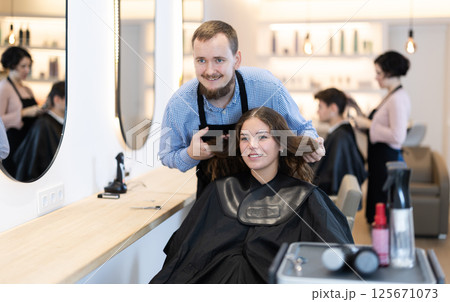 Young man barbershop employee stands next to female client, discussing details of haircut Young man barbershop employee stands next to female client, discussing details of haircut 125671073