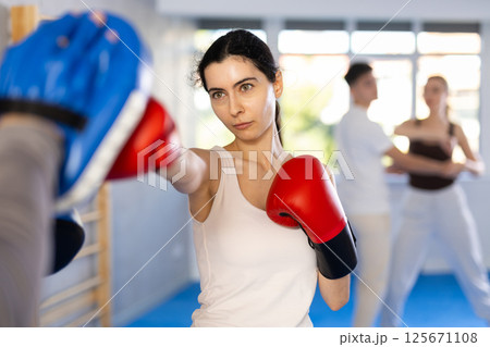 Young girl training boxing kicks on punch mitts held by instructor 125671108