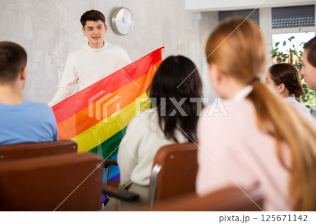 Young male professor showing rainbow flag to group of students 125671142