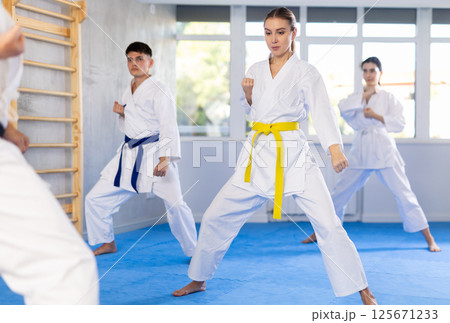 Young woman attendee of karate classes practicing kata standing in row with others 125671233