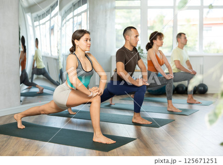 Young woman with multinational group of sporty adult people training stretching workout in yoga studio Young woman with multinational group of sporty adult people training stretching workout in yoga studio 125671251