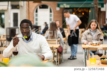 African man sits on terrace of a restaurant and eats 125671488