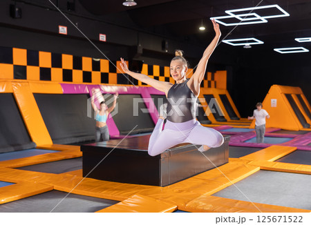 Middle-aged woman in sport clothes high jumping in trampoline arena 125671522