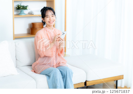 部屋でスマホを操作する若い女性 125671837