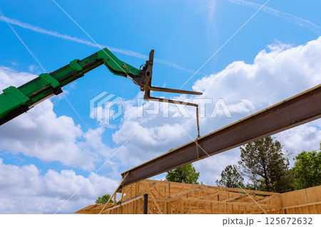 Heavy crane telehandler is lifting steel beam at construction site, ongoing building activity. 125672632