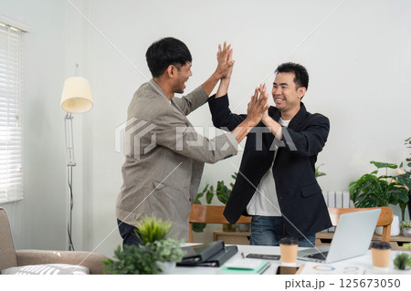 Business Collaboration and Success. Two professionals celebrating a successful partnership in a modern office setting. 125673050