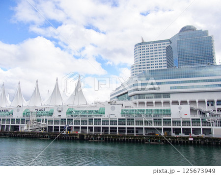 カナダプレイスの建物越しに雲の合間から青空がのぞく曇り空のウォーターフロント風景 125673949