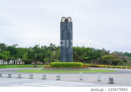曇り空の下、平和祈念公園のひめゆりの塔と足元に広がる赤と黄色の花、緑豊かな草と木々の風景 曇り空の下、平和祈念公園のひめゆりの塔と足元に広がる赤と黄色の花、緑豊かな草と木々の風景 125673963