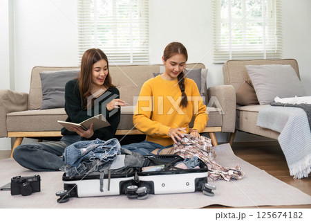 Companions Preparing for Travel: Young women packing a suitcase Companions Preparing for Travel: Young women packing a suitcase 125674182