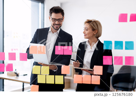 Team of male and female professionals collaborating on brainstorm with sticky notes, modern workspace Team of male and female professionals collaborating on brainstorm with sticky notes, modern workspace 125676180