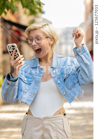 Excited European woman using mobile phone typing browsing celebrating win on urban city street Excited European woman using mobile phone typing browsing celebrating win on urban city street 125677033
