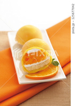 Close-up of a yellow mochi with a white layer and orange jam inside. Served with an orange slice. Close-up of a yellow mochi with a white layer and orange jam inside. Served with an orange slice. 125677042