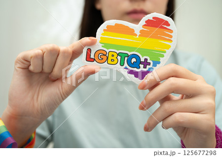 Asian lady wearing rainbow flag wristbands and hold red heart, symbol of LGBT pride month celebrate annual in June social of gay, lesbian, bisexual, transgender, human rights. 125677298