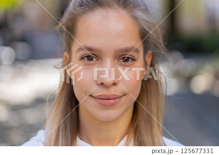 Closeup portrait of young Caucasian woman tourist teenager smiling looking at camera on city street Closeup portrait of young Caucasian woman tourist teenager smiling looking at camera on city street 125677331