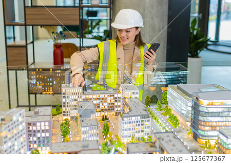 Confident architect in hardhat using smartphone while analyzing office complex model at workplace Confident architect in hardhat using smartphone while analyzing office complex model at workplace 125677367