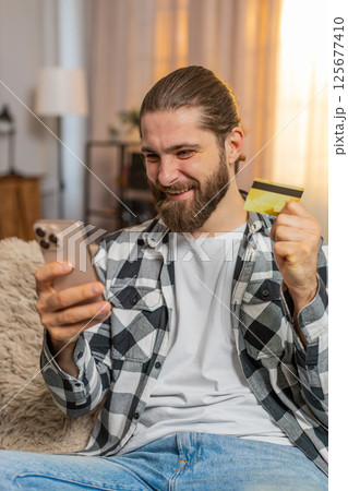 Young man paying with credit card at home, phone purchase, sofa check, nod ok, confident secure vibe Young man paying with credit card at home, phone purchase, sofa check, nod ok, confident secure vibe 125677410