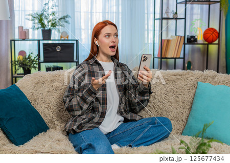 Woman sitting on sofa learning new language with mobile app speaking words out loud with focus joy 125677434