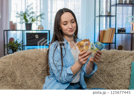 Young woman happily counting pile of cash euro bills on sofa celebrating wealth successful finance Young woman happily counting pile of cash euro bills on sofa celebrating wealth successful finance 125677445
