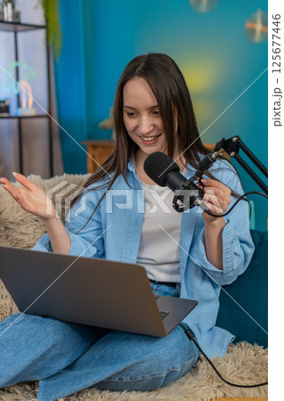 Woman blogger happily recording podcast vlog on sofa actively gesturing telling interesting story 125677446