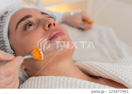 Enzyme therapy beautician applying moisturizing medical cream on young adult woman face with brushes 125677461